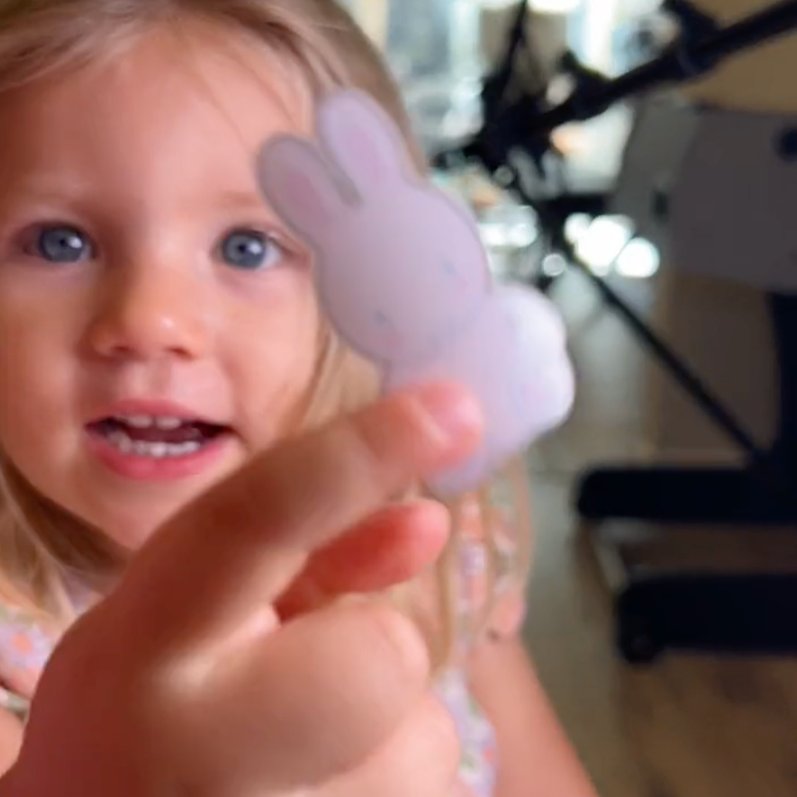 Child holding a small purple object with a blurred indoor background sticker toy